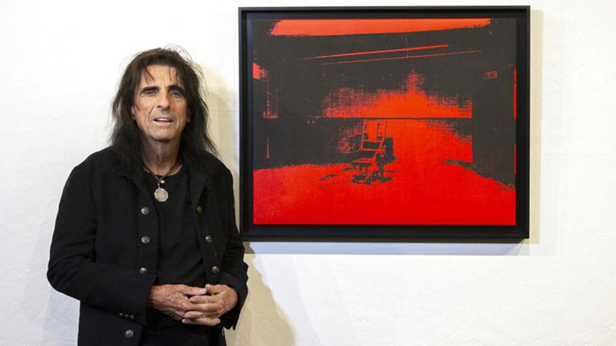 In this photo provided by Chris Loomis, singer Alice Cooper stands by his Andy Warhol red acrylic and silkscreen on canvas called "Little Electric Chair" at the Larsen Gallery in Scottsdale, Ariz., on Wednesday, May 12, 2021. The Warhol canvas found years ago in the garage of rocker Alice Cooper could become the highest selling artwork ever in Arizona. The music legend, who has a home in metro Phoenix, announced Thursday, May 13, 2021, that he would auction off "Little Electric Chair." The gallery estimates it could fetch anywhere from $2.5 million to $4.5 million.