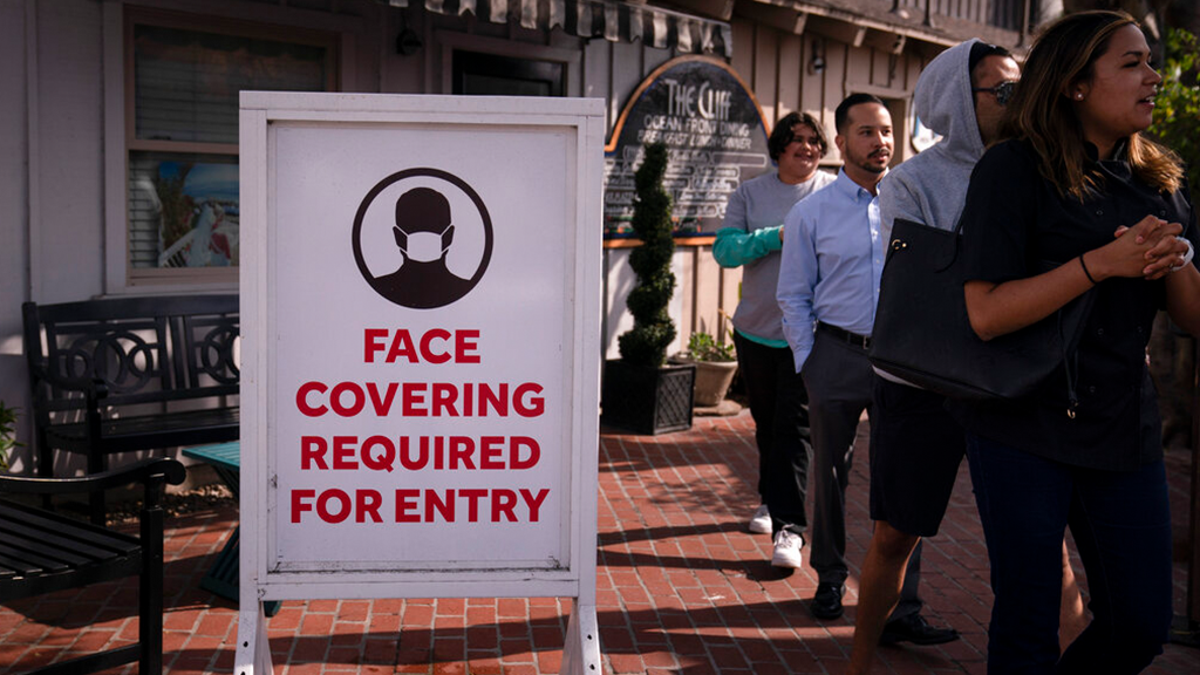 People walk past a sign requesting customers to wear masks in Laguna Beach, California, Monday, May 17, 2021. 