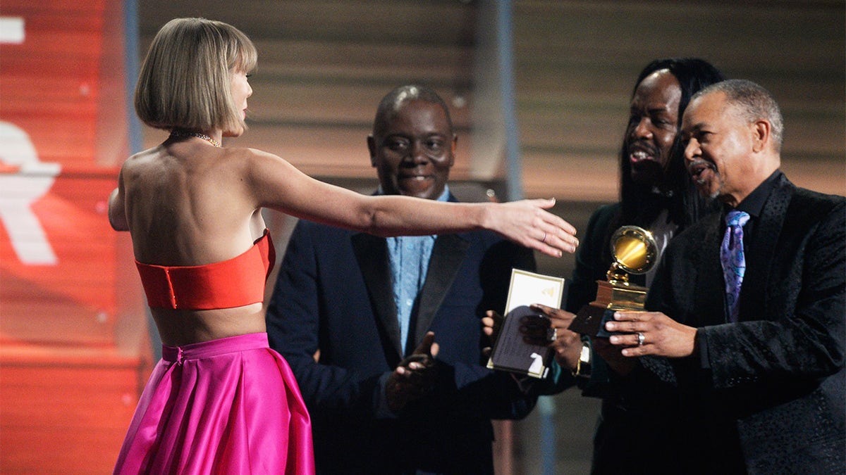 Singer Taylor Swift (C) accepts the Album of the Year award for ‘1989’ onstage from musicians (L-R) Philip Bailey, Verdine White and Ralph Johnson of Earth, Wind &amp; Fire during The 58th GRAMMY Awards at Staples Center on February 15, 2016, in Los Angeles, California. 