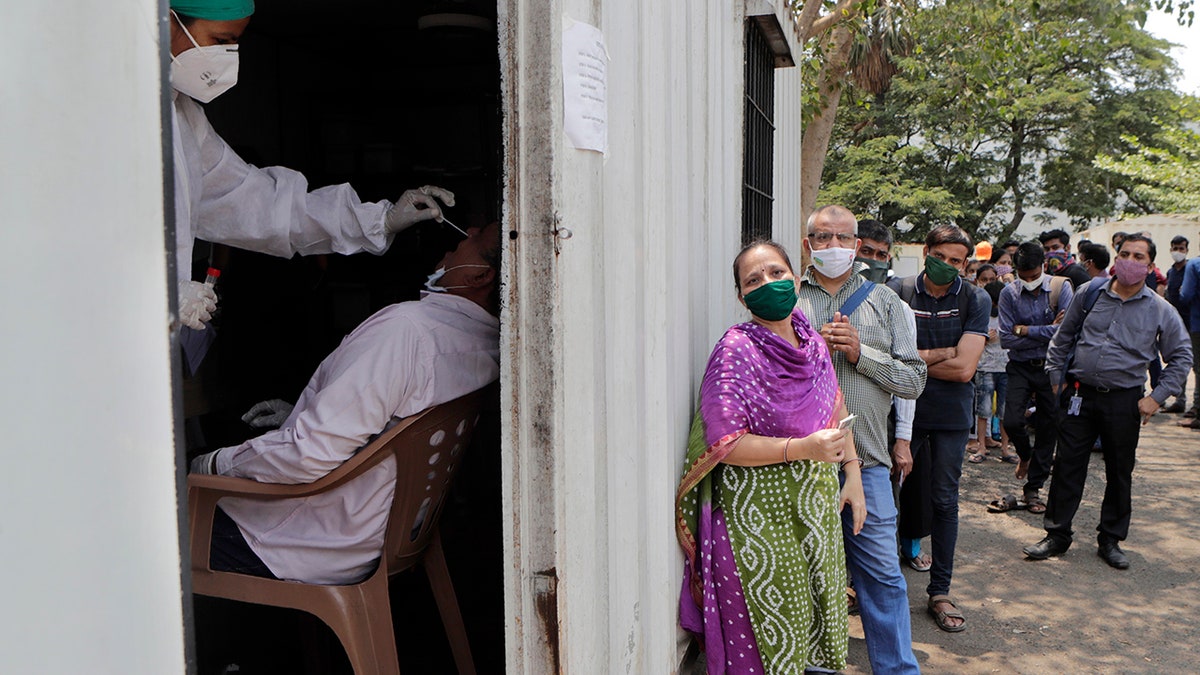 May 6, 2021: In this file photo, a health worker takes a nasal swab sample of a person to test for COVID-19 as others wait for their turn outside a field hospital in Mumbai, India. 
