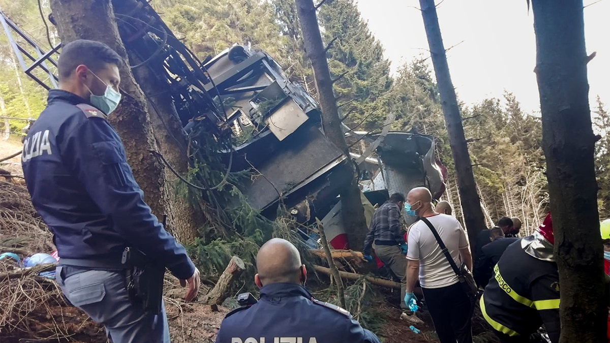 Rescuers work by the wreckage of a cable car after it collapsed near the summit of the Stresa-Mottarone line in the Piedmont region, northern Italy, Sunday, May 23, 2022. A cable car taking visitors to a mountaintop view of some of northern Italy's most picturesque lakes plunged to the ground Sunday, killing at least nine people and sending two children to the hospital, authorities said. (Italian Police via AP)