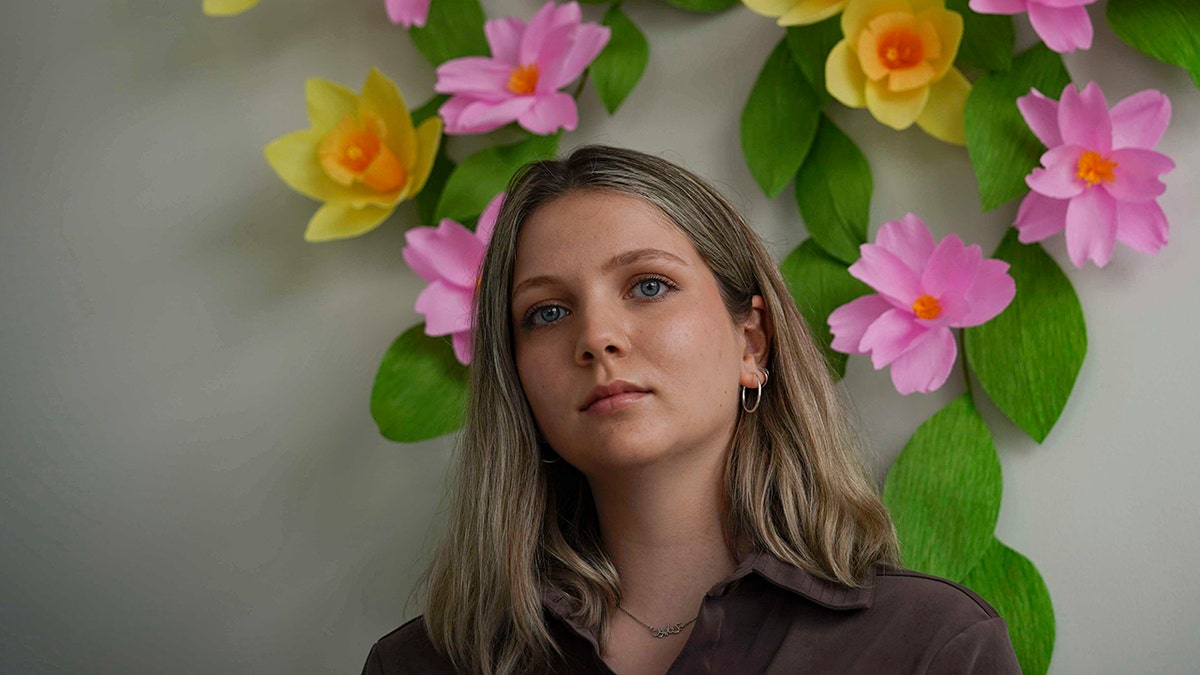 Artist and puppeteer Katayoun Amir-Aslani stands for a portrait next to her floral art creation in New York on Friday, April 9, 2021. The artwork signals "re-birth and new beginnings," said Amir-Aslani. Balance, harmony and wholeness. That's how I feel now." Amir-Aslani left Gettysburg College after a sexual assault in the spring of 2014. (AP Photo/Bebeto Matthews)