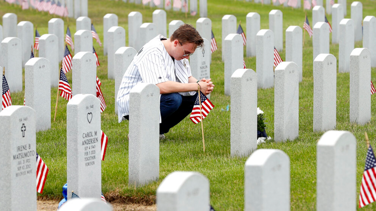 A man kneels at a grave on Memorial Day