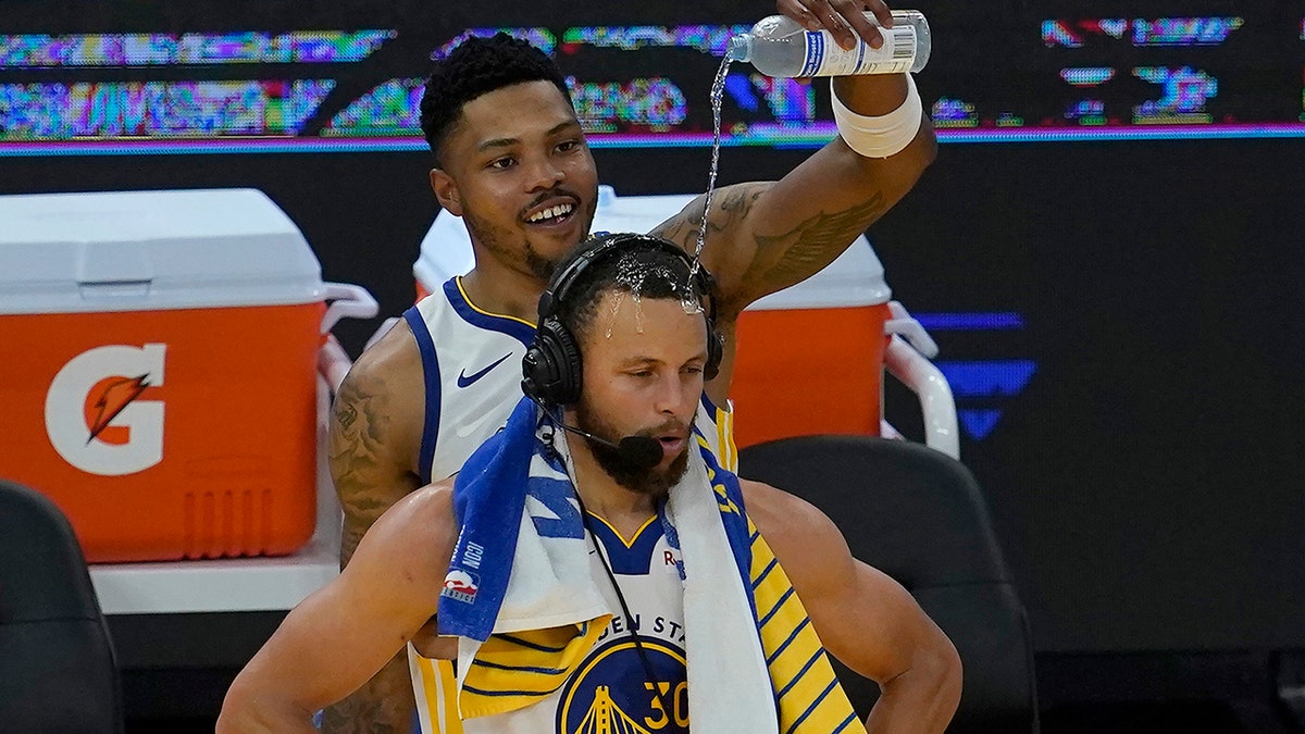 Golden State Warriors forward Kent Bazemore, top, pours water on the head of guard Stephen Curry after an NBA basketball game against the Memphis Grizzlies in San Francisco, Sunday, May 16, 2021.