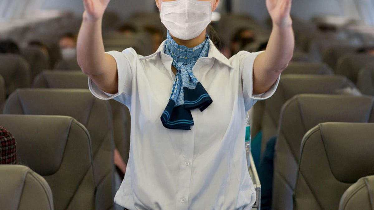 Flight attendant showing the emergency exit in an airplane wearing a facemask