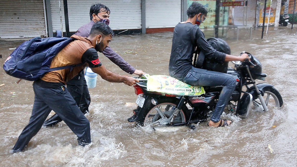 Two men help a motorist to wade through a waterlogged street after heavy rains in Ahmedabad, India, Tuesday, May 18, 2021. Cyclone Tauktae, the most powerful storm to hit the region in more than two decades, packed sustained winds of up to 210 kilometers (130 miles) per hour when it came ashore in Gujarat state late Monday. (AP Photo/Ajit Solanki)