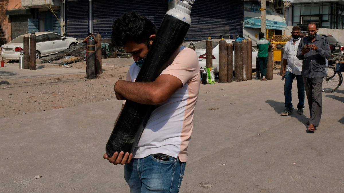 May 3, 2021: A man walks carrying a refilled cylinder as family members of COVID-19 patients wait in line to refill their oxygen cylinders at Mayapuri area in New Delhi, India. 
