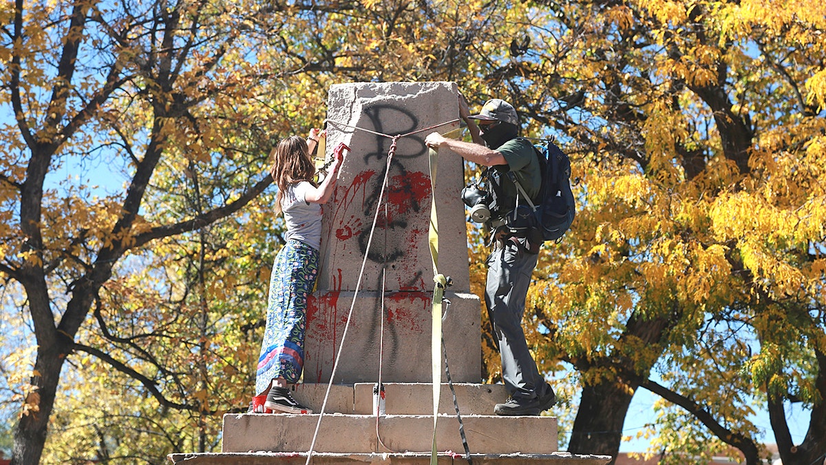 Demonstrators secure a rope around the centerpiece of a solid stone obelisk before tearing it down in Santa Fe, New Mexico, Oct. 12, 2020. (Associated Press)