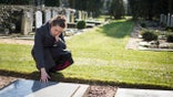 Woman sitting at grave with hand on grave