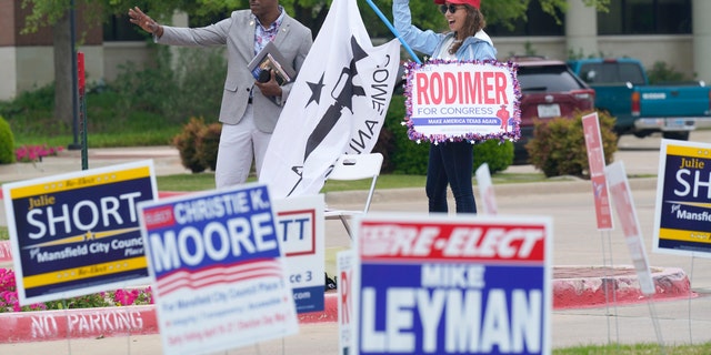 R.C. Maxwell, left, and Leah Kortre wave to voters arriving to cast their ballot during early voting Tuesday, April 27, 2021, in Mansfield, Texas. (AP Photo/LM Otero)