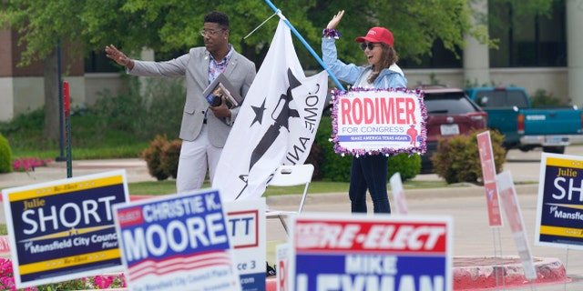 R.C. Maxwell, left, and Leah Kortre wave to voters arriving to cast their ballot during early voting Tuesday, April 27, 2021, in Mansfield, Texas. (AP Photo/LM Otero)