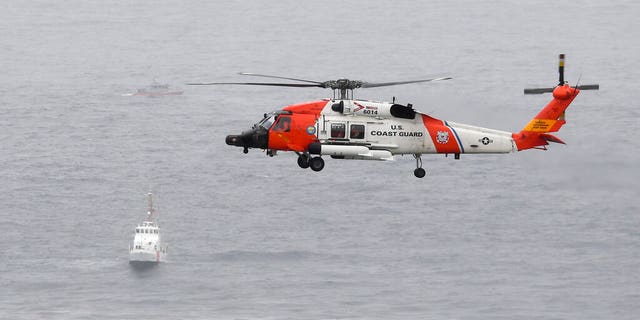 A U.S. Coast Guard helicopter flies over boats searching the area where a boat capsized just off the San Diego coast.