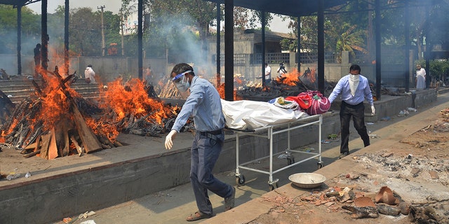 Relatives carry the body of a person who died of COVID-19 as multiple pyres of other COVID-19 victims burn at a crematorium in New Delhi, India on May 1, 2021. (AP Photo/Amit Sharma, File)