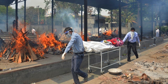 Relatives carry the body of a person who died of COVID-19 as multiple pyres of other COVID-19 victims burn at a crematorium in New Delhi, India on May 1, 2021. (AP Photo/Amit Sharma, File)