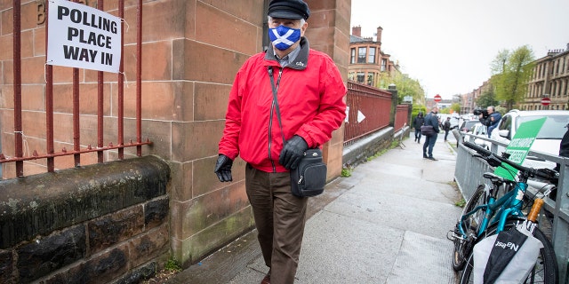 A man wearing a face mask arrives to vote at a polling station in Glasgow, Scotland, Thursday May 6, 2021.