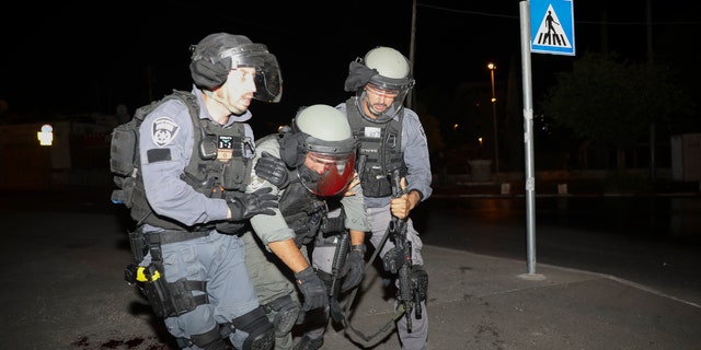 An injured Israeli police officer is helped during clashes with Palestinian protesters, in east Jerusalem, Friday, May 7, 2021. Palestinians protested following Israel's threatened eviction of dozens of Palestinians in the Sheikh Jarrah neighborhood in east Jerusalem, who have been embroiled in a long legal battle with Israeli settlers trying to acquire property in the neighborhood. (AP Photo/Mahmoud Illean)