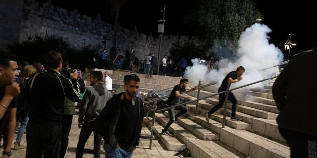 Palestinians react to stun grenades fired by Israeli police to clear the Damascus Gate to the Old City of Jerusalem after clashes at the Al-Aqsa Mosque compound, Friday, May 7, 2021. Palestinian worshippers clashed with Israeli police late Friday at the holy site sacred to Muslims and Jews.