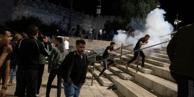 Palestinians react to stun grenades fired by Israeli police to clear the Damascus Gate to the Old City of Jerusalem after clashes at the Al-Aqsa Mosque compound, Friday, May 7, 2021. Palestinian worshippers clashed with Israeli police late Friday at the holy site sacred to Muslims and Jews.