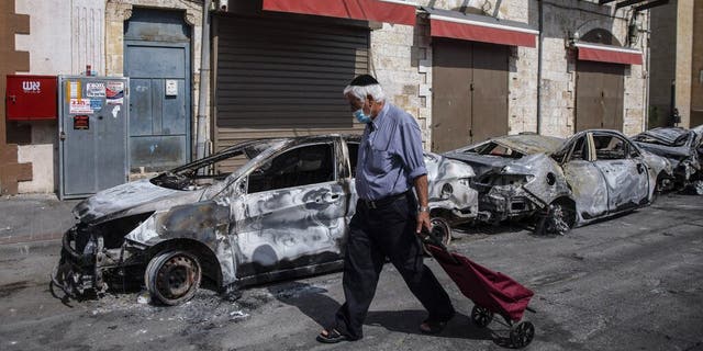 A man passes by cars torched after a night of violence between Israeli Arab protesters and Israeli police in the mixed Arab-Jewish town of Lod, central Israel, Tuesday, May 11, 2021. (AP Photo/Heidi Levine)