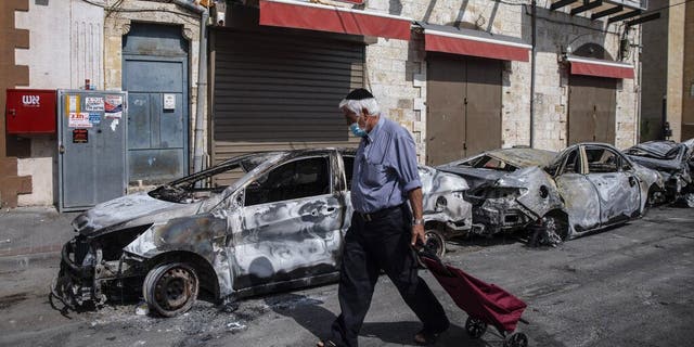 A man passes by cars torched after a night of violence between Israeli Arab protesters and Israeli police in the mixed Arab-Jewish town of Lod, central Israel, Tuesday, May 11, 2021. (AP Photo/Heidi Levine)