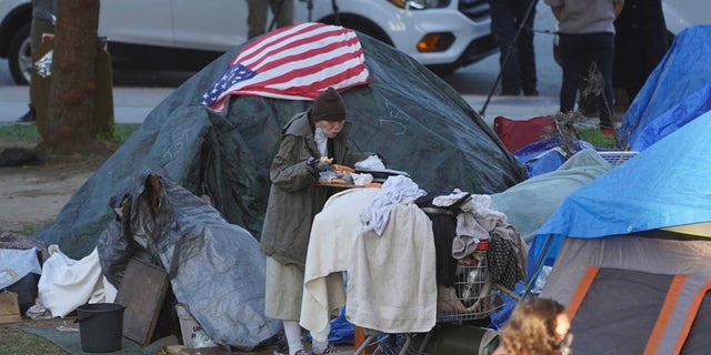 In this March 24, 2021, file photo a woman eats at her tent at the Echo Park homeless encampment at Echo Park Lake in Los Angeles.  (AP Photo/Damian Dovarganes)