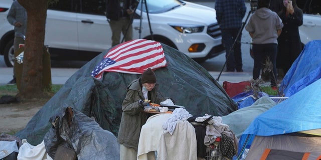 In this March 24, 2021, file photo a woman eats at her tent at the Echo Park homeless encampment at Echo Park Lake in Los Angeles. (AP Photo/Damian Dovarganes)
