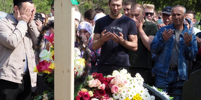 People pray next to the grave of Elvira Ignatieva, an English language teacher who was killed at a school shooting on Tuesday in Kazan, Russia, Wednesday, May 12, 2021. Russian officials say a gunman attacked a school in the city of Kazan and Russian officials say several people have been killed. Officials said the dead in Tuesday's shooting include students, a teacher and a school worker. Authorities also say over 20 others have been hospitalised with wounds. (AP Photo/Dmitri Lovetsky)