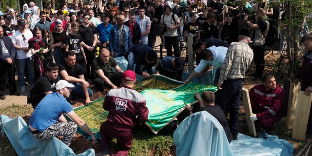 People gather next to the grave during a funeral of Elvira Ignatieva, an English language teacher who was killed at a school shooting on Tuesday, in Kazan, Russia, Wednesday, May 12, 2021. Russian officials say a gunman attacked a school in the city of Kazan and Russian officials say several people have been killed. Officials said the dead in Tuesday's shooting include students, a teacher and a school worker. Authorities also say over 20 others have been hospitalised with wounds. (AP Photo/Dmitri Lovetsky)