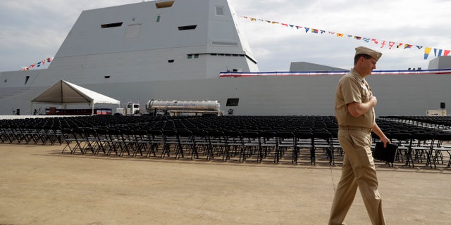 A member of the U.S. Navy walks past the future USS Zumwalt in Baltimore, in this Thursday, Oct. 13, 2016, file photo. The electric-drive, angular Zumwalt was commissioned into service, but its 155mm advanced gun system is being scrapped because its munitions are too expensive. (AP Photo/Patrick Semansky, File)