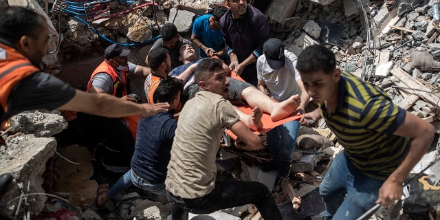 FILE - In this May 16, 2021, file photo, Palestinians rescue a survivor from the rubble of a destroyed residential building following deadly Israeli airstrikes in Gaza City. The Gaza Strip's already feeble health system is being brought to its knees by the fourth war in just over a decade. (AP Photo/Khalil Hamra, File)