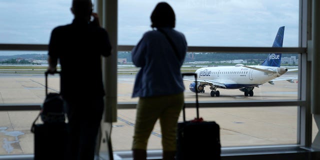 Travelers watch a JetBlue Airways aircraft taxi away from a gate at Ronald Reagan Washington National Airport ahead of Memorial Day weekend, Tuesday, May 25, 2021, in Arlington, Va. (AP Photo/Patrick Semansky)