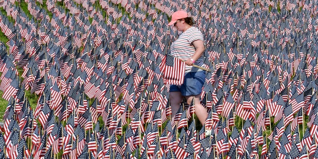 A volunteer walks through a field of American flags planted on Boston Common Wednesday, May 26, 2021, in Boston. (AP Photo/Josh Reynolds)