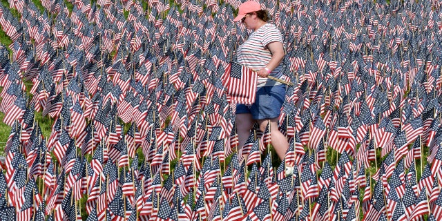 A volunteer walks through a field of American flags planted on Boston Common Wednesday, May 26, 2021, in Boston. (AP Photo/Josh Reynolds)