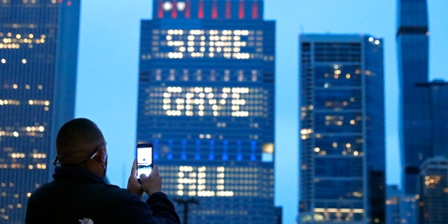 A person takes a photo, Sunday, May 30, 2021, of an illuminated sign on Chicago's Blue Cross Blue Shield Tower displaying "Some Gave All" in honor of Memorial Day. (AP Photo/Shafkat Anowar)