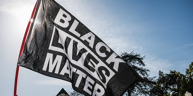 LOS ÁNGELES, CALIFORNIA, ESTADOS UNIDOS - 2021/04/20: Un manifestante ondea una bandera de Black Lives Matter durante la manifestación.  Horas después del veredicto del juicio de Derek Chauvin, los manifestantes se reúnen frente a la casa del alcalde de Los Ángeles, Eric Garcetti, para protestar por su propuesta de financiación del Departamento de Policía de Los Ángeles.