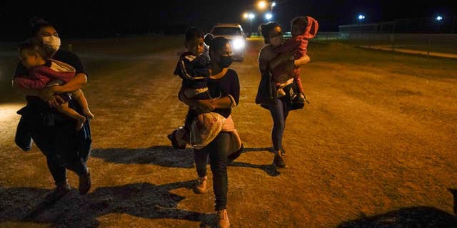 Migrant women carry children in the rain at an intake area after turning themselves in upon crossing the U.S.-Mexico border, late Tuesday, May 11, 2021, in La Joya, Texas.  (AP Photo/Gregory Bull)