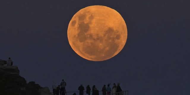 SYDNEY, AUSTRALIA - MAY 26: People watch the "Super Flower Blood Moon" rises over the Pacific Ocean at Bondi Beach in Sydney, Australia on May 26, 2021. The "Super" moon observed in May is often defined as "flower moon" as well, mainly due to association with flowers blooming at this time of year. During the eclipse, the moon turns into a deep blood-red color, known as "blood moon." This celestial incident -- known as "Super Flower Blood Moon" -- is the only full lunar eclipse of this year. (Photo by Steven Saphore/Anadolu Agency via Getty Images)