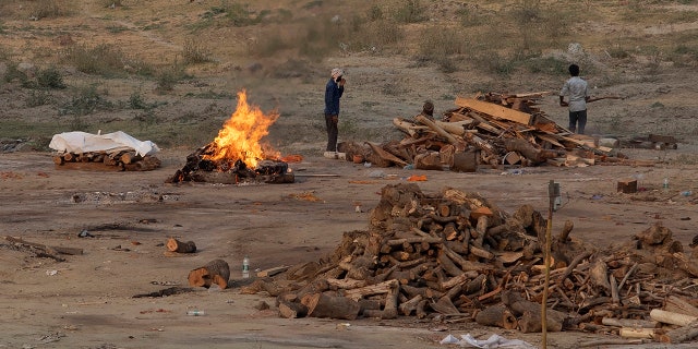 May 1, 2021: Body of a COVID-19 victim lies covered in white cloth next to a burning pyre of another victim at a cremation ground in Prayagraj, India.