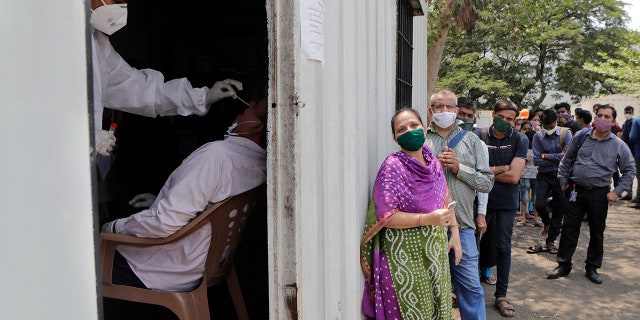 May 6, 2021: In this file photo, a health worker takes a nasal swab sample of a person to test for COVID-19 as others wait for their turn outside a field hospital in Mumbai, India.