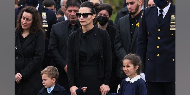Irene Tsakos holds the hands of her children as she watches NYPD officers fold an American flag that draped the casket of her husband NYPD Officer Anastasios Tsakos during his funeral service at St. Paraskevi Greek Orthodox Shrine Church on May 04, 2021 in Greenlawn, New York.