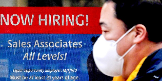 A man walks past a "Now Hiring" sign in front of a store on December 1, 2020 in Arlington, Virginia. (Photo by OLIVIER DOULIERY/AFP via Getty Images)