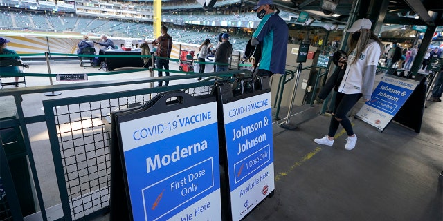 Seattle Mariners fans walk past signs for the Johnson & Johnson and Moderna COVID-19 vaccines, Tuesday, May 4, 2021, during a clinic held at T-Mobile Park before a baseball game between the Mariners and the Baltimore Orioles in Seattle. (AP Photo/Ted S. Warren)