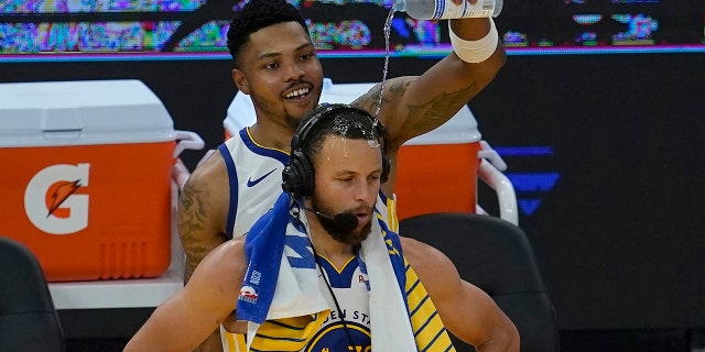 Golden State Warriors forward Kent Bazemore, top, pours water on the head of guard Stephen Curry after an NBA basketball game against the Memphis Grizzlies in San Francisco, Sunday, May 16, 2021.