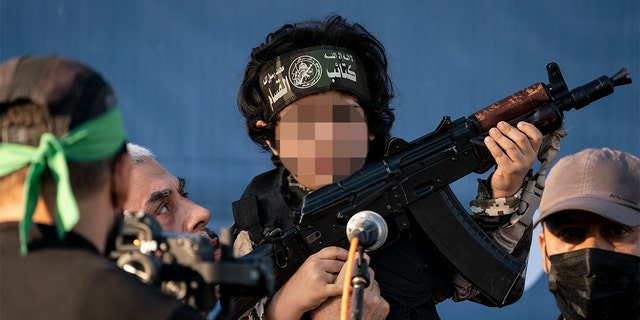 Yahya Sinwar, Palestinian leader of Hamas in the Gaza Strip, second left, holds a child in a soldier costume, on stage with a weapon for the cameras, at a rally of supporters days after a cease-fire was reached in an 11-day war between Gaza's Hamas rulers and Israel, Monday. (AP Photo/John Minchillo)