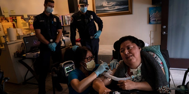 May 12, 2021: Pharmacist Stella Kim, foreground left, administers the second dose of the Pfizer COVID-19 vaccine to Socorro Franco-Martinez, who suffers from muscular dystrophy, in her apartment as Torrance firefighters, Trevor Borello, rear left, and Alessandro Demuro watch in Torrance, Calif. 