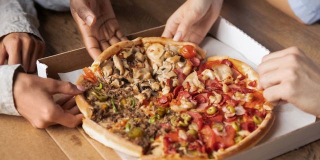 Close up of hands sharing slices of meat pizza.