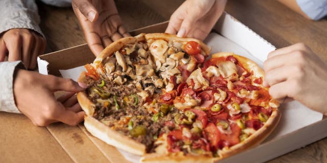 Close up of hands sharing slices of meat pizza.