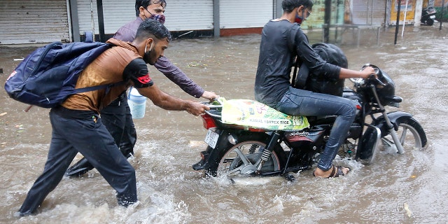Two men help a motorist wade through a waterlogged street after heavy rains in Ahmedabad, India on Tuesday, May 18, 2021. Cyclone Tauktae, the most powerful storm to hit the region in more than two decades, resulted in sustained winds of up to 210 kilometers (130 miles) per hour when it made landfall in Gujarat state on Monday evening. (AP Photo / Ajit Solanki)