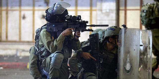 An Israeli soldier aims his weapon while others take cover behind their shields during a Palestinian protest amid a flare-up of Israeli-Palestinian violence, in Hebron in the Israeli-occupied West Bank May 11, 2021. 