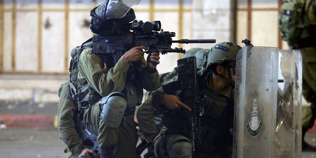 An Israeli soldier aims his weapon while others take cover behind their shields during a Palestinian protest amid a flare-up of Israeli-Palestinian violence, in Hebron in the Israeli-occupied West Bank May 11, 2021.
